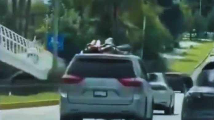 Dos mujeres viajando completamente acostadas sobre el techo de una minivan gris en movimiento sobre la Vía Atlixcáyotl en Puebla.